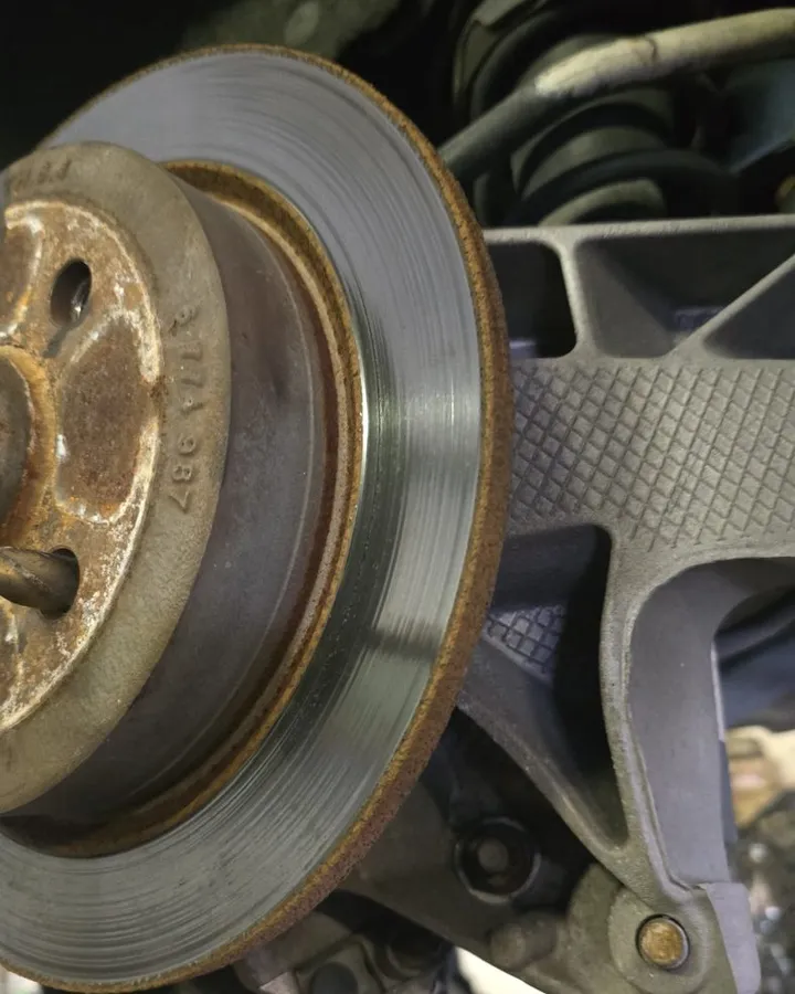 A worn brake rotor and caliper on a car in the Front Line Auto bay