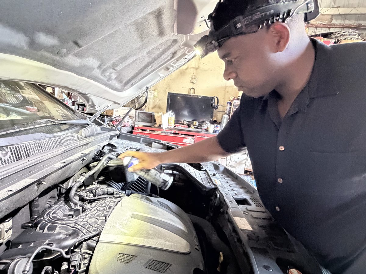 Front Line Auto technician using a headlamp to inspect an engine bay in Oakland Park